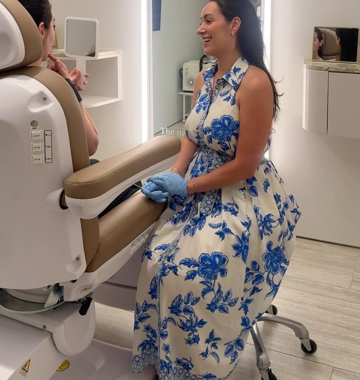 Nadia in a blue floral dress talking with a client seated in the treatment chair